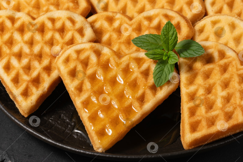 Скачать Вкусные вафли в форме сердца с сиропом и мятой на черной тарелке, идеально подходящие для завтрака или десерта фотосток Ozero
