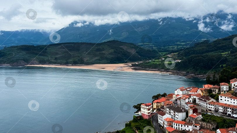 Скачать Прибрежная деревня с красными крышами с видом на спокойный залив и пышные холмы фотосток Ozero