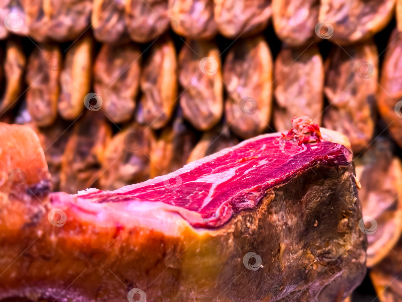 Скачать Крупный план вяленой ветчины в камере выдержки на фоне подвешенного мяса фотосток Ozero