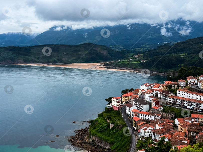 Скачать Живописная прибрежная деревушка с красными крышами и видом на тихий залив и горы фотосток Ozero