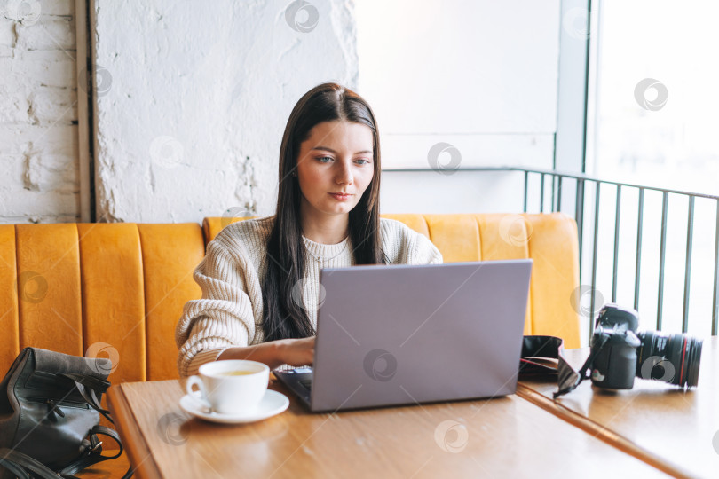 Скачать Брюнетка, улыбающаяся молодая женщина-фотограф, работает со своей камерой и ноутбуком в кафе фотосток Ozero