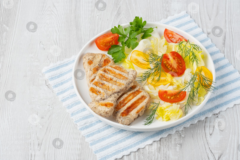 Скачать Полезный кето-ланч с куриным мясом на гриле и экологически чистыми помидорами и зеленью. Запеченная куриная грудка, филе и салат из свежих овощей на белом деревянном столе, copy space фотосток Ozero