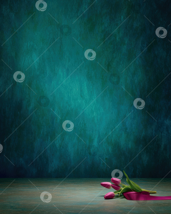 Скачать Яркие розовые тюльпаны с зелеными листьями и атласной лентой расположены на текстурированной поверхности на насыщенном бирюзовом фоне, создавая безмятежную и элегантную цветочную композицию фотосток Ozero