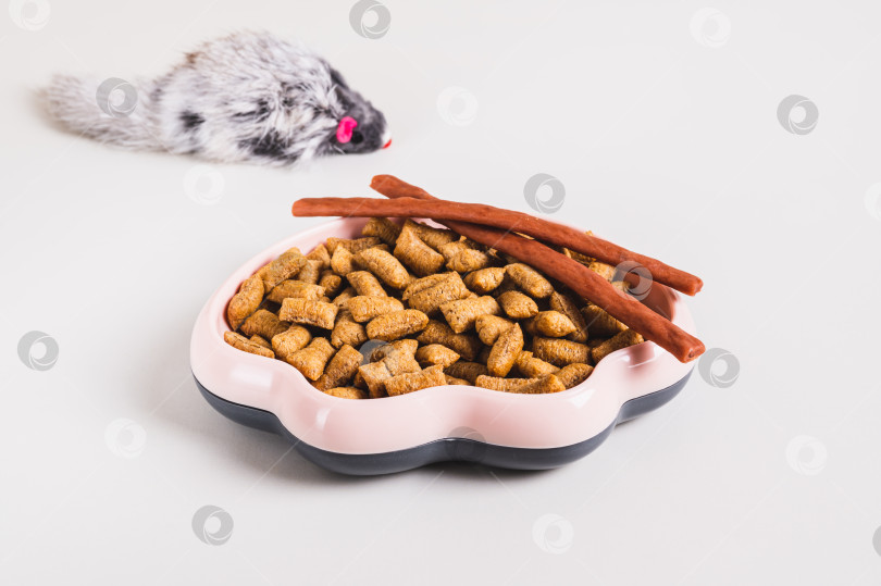 Скачать Миска с гранулами сухого кошачьего корма и игрушечная пушистая мышка на столе фотосток Ozero
