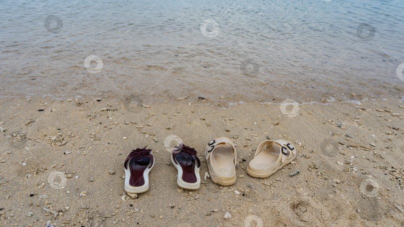 Скачать Две пары шлепанцев на песчаном пляже у кромки воды. фотосток Ozero