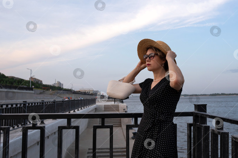 Скачать Женщина поправляет соломенную шляпу, стоя у перил набережной. фотосток Ozero