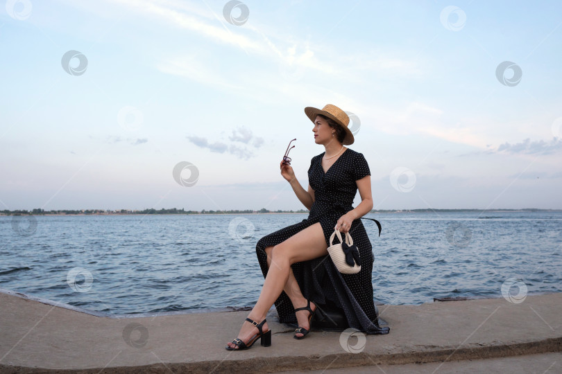 Скачать Женщина в платье в горошек смотрит на море, держа в руках солнцезащитные очки. фотосток Ozero