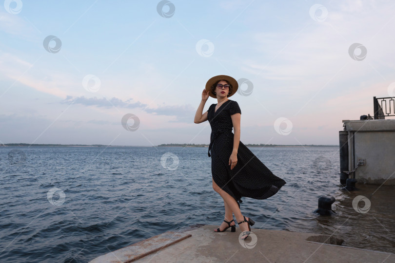 Скачать Женщина в черном платье позирует у океана на закате. фотосток Ozero