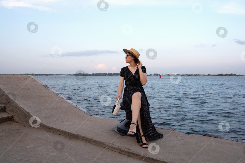 Скачать Женщина в платье в горошек сидит на пирсе на закате. фотосток Ozero