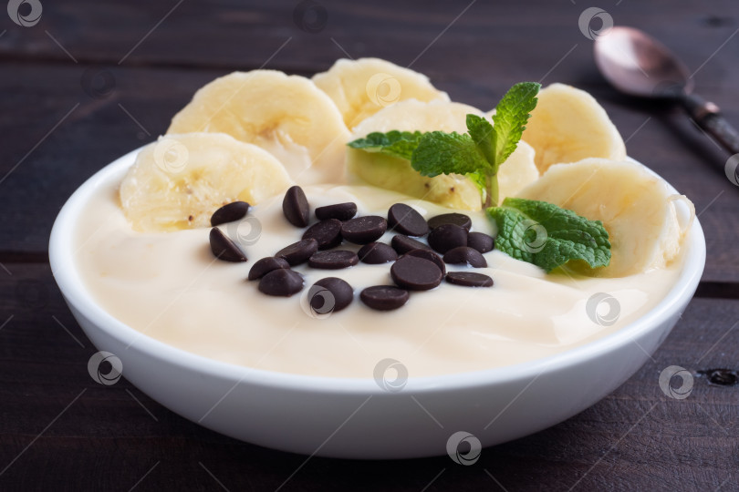 Скачать Полезный завтрак, десерт с молоком, йогуртом, бананом и шоколадом на тарелке. Фон из темного дерева. фотосток Ozero