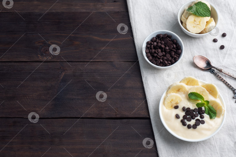 Скачать Полезный завтрак, десерт с молоком, йогуртом, бананом и шоколадом на тарелке. Фон из темного дерева. Вид сверху, свободное место для копирования. фотосток Ozero