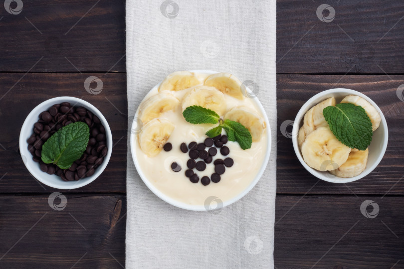 Скачать Полезный завтрак, десерт с молоком, йогуртом, бананом и шоколадом на тарелке. На фоне темного дерева. Вид сверху фотосток Ozero