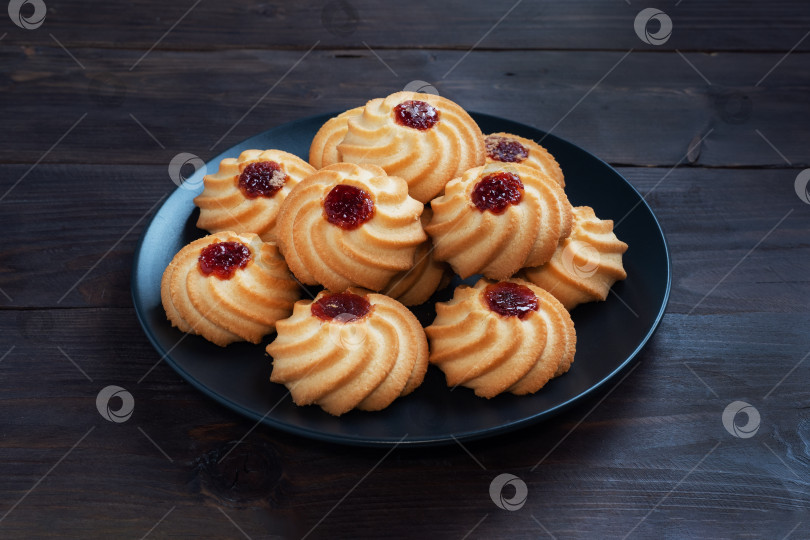 Скачать Песочное печенье "Курабье" с ягодным джемом в черной тарелке. Восхитительный десерт на фоне темного дерева с пространством для копирования. фотосток Ozero