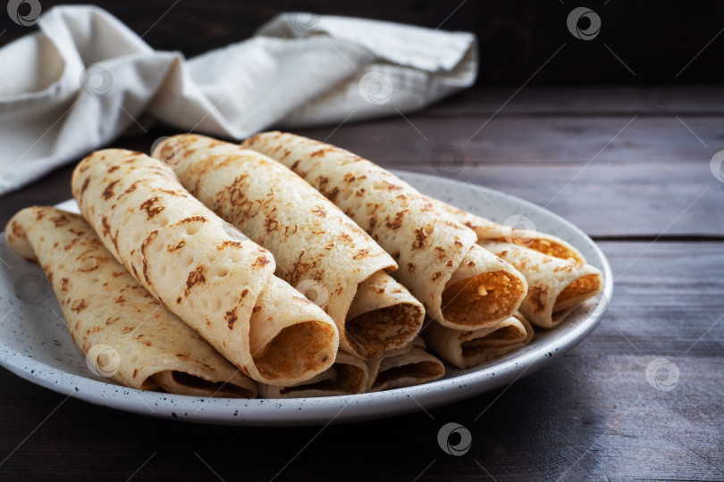 Скачать Тонкие блинчики, скрученные в рулет на тарелке. Концепция вкусного завтрака или масленицы. деревянный фон. фотосток Ozero