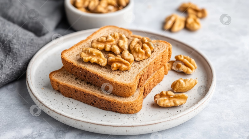 Скачать Ломтики цельнозернового хлеба, посыпанные грецкими орехами, выложите на текстурированную тарелку, а рядом поставьте миску с грецкими орехами фотосток Ozero