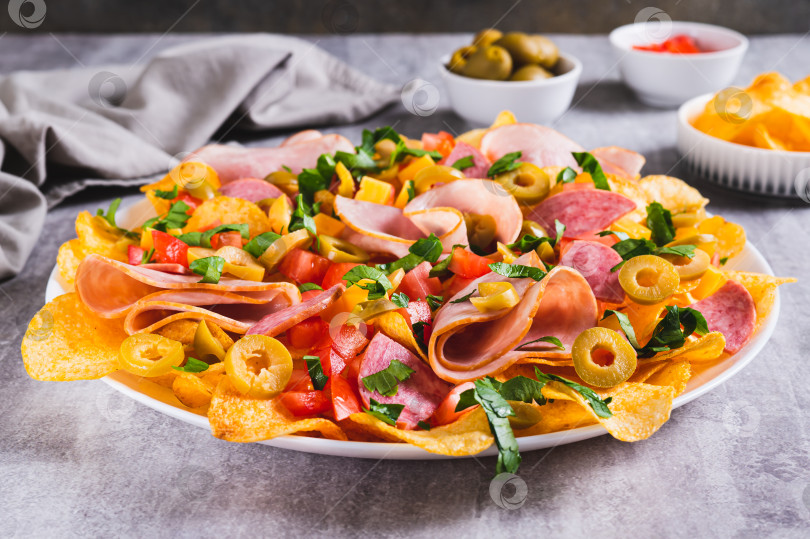 Скачать Мясные начос с чипсами, салями, сыром и оливками на тарелке на столе фотосток Ozero