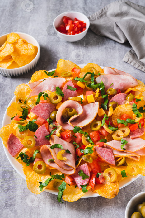 Скачать Трендовые закуски - начос из мясной нарезки с картофельными чипсами на тарелке на столе в вертикальном положении фотосток Ozero
