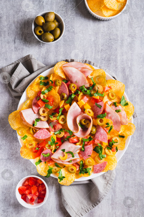 Скачать Трендовая закуска - начос из мясной нарезки с картофельными чипсами на тарелке, расположенной на столешнице в вертикальном положении фотосток Ozero