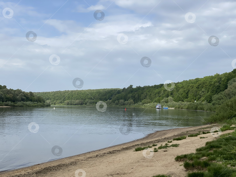 Скачать Речной пейзаж со спокойной водой, песчаным пляжем и пышными лесами на фоне облачного неба фотосток Ozero