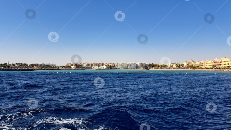 Скачать Потрясающий вид на спокойные голубые океанские волны, мягко набегающие на песчаный пляж, и яркие прибрежные здания под ясным голубым небом. Красное море. Хургада. Египет фотосток Ozero