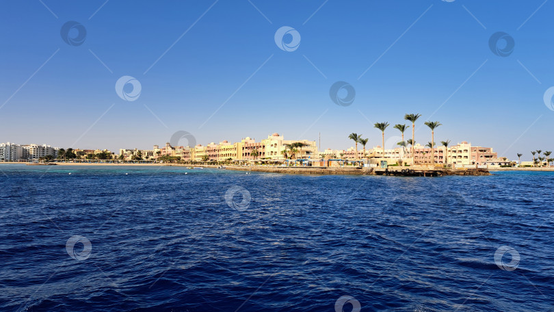 Скачать Вид на прибрежный курорт с пальмами и чистыми голубыми водами под ясным небом, создающий спокойную атмосферу отдыха и манящий пейзаж. Красное море. Хургада. Египет фотосток Ozero