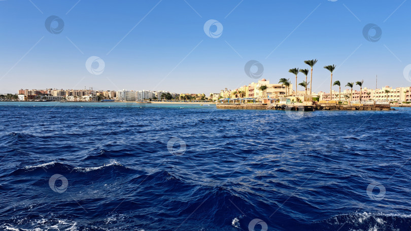 Скачать Захватывающий вид на побережье со спокойными голубыми водами, мягко покачивающимися пальмами и живописной береговой линией со зданиями под ясным голубым небом, создающими безмятежную атмосферу. Красное море. Хургада. Египет фотосток Ozero