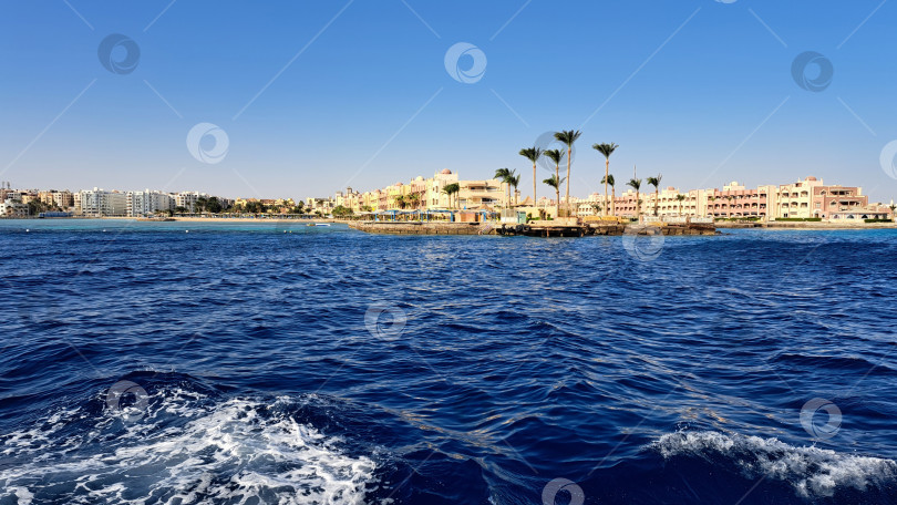Скачать Живописный вид на побережье с яркими зданиями и пальмами вдоль береговой линии, с чистыми голубыми водами и пологими волнами, создающими спокойную атмосферу. Красное море. Хургада. Египет фотосток Ozero
