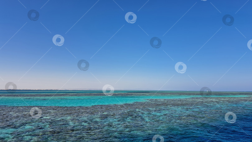 Скачать Потрясающий вид на спокойные бирюзовые воды, встречающиеся с чистым голубым небом, демонстрирующие безмятежный океанский пейзаж и яркие коралловые рифы под поверхностью. Красное море. Хургада. Египет фотосток Ozero