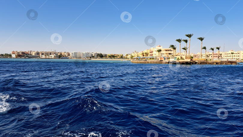 Скачать Захватывающий вид на побережье, демонстрирующий спокойные голубые воды, пальмы и красочные здания вдоль береговой линии под ясным голубым небом, создающий безмятежную тропическую атмосферу. Красное море. Хургада. Египет фотосток Ozero