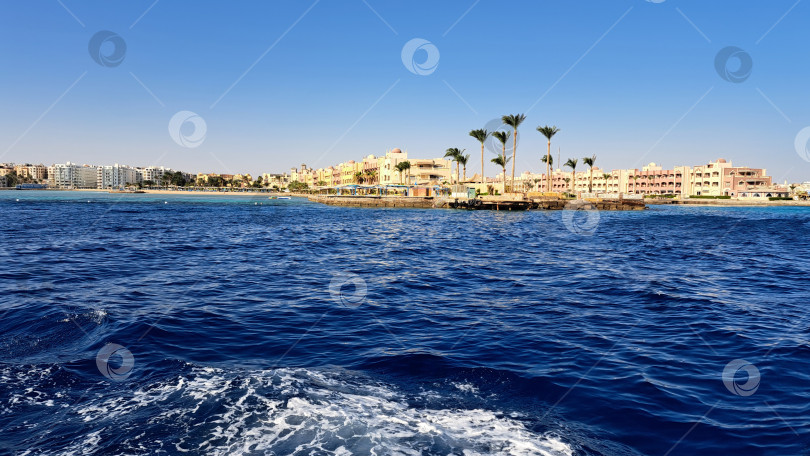 Скачать Захватывающий вид на побережье, с прозрачными голубыми водами и пальмами, с отдаленным курортом и зданиями под ярким солнечным небом, создающими атмосферу тропического рая. Красное море. Хургада. Египет фотосток Ozero