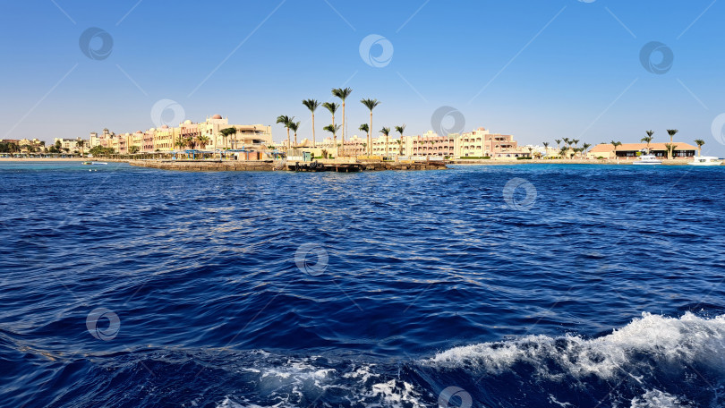 Скачать Живописный вид на побережье с яркими зданиями вдоль берега, окруженными пальмами и чистыми голубыми водами, создает спокойную атмосферу для отдыха. Красное море. Хургада. Египет фотосток Ozero