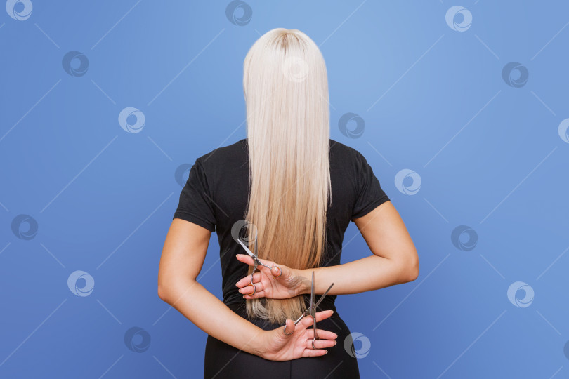 Скачать Женщина с ножницами в руках стоит в стороне и подстригает свои длинные светлые волосы.  фотосток Ozero