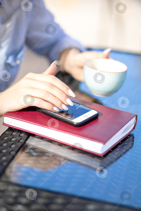 Скачать мобильный телефон в руках женщины. женщина разговаривает по телефону. на заднем плане - стол и дневник фотосток Ozero