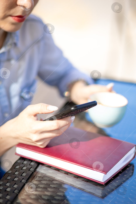 Скачать мобильный телефон в руках женщины. женщина разговаривает по телефону. на заднем плане - стол и дневник фотосток Ozero