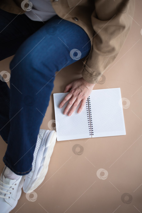 Скачать Вид сверху: Молодая женщина-фрилансер сидит на полу, рядом с открытым блокнотом. Концепция комфортной работы на дому. фотосток Ozero