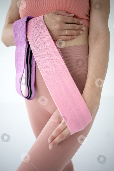 Скачать Фитнес-резинки для занятий спортом в руках девушки. На снимке крупным планом женские руки натягивают синюю спортивную резинку для тренировки мышц тела в тренажерном зале фотосток Ozero