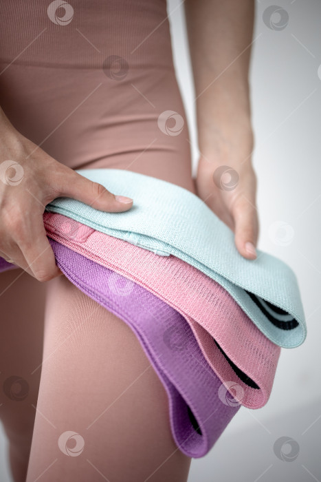 Скачать Фитнес-резинки для занятий спортом в руках девушки. На снимке крупным планом женские руки натягивают синюю спортивную резинку для тренировки мышц тела в тренажерном зале фотосток Ozero