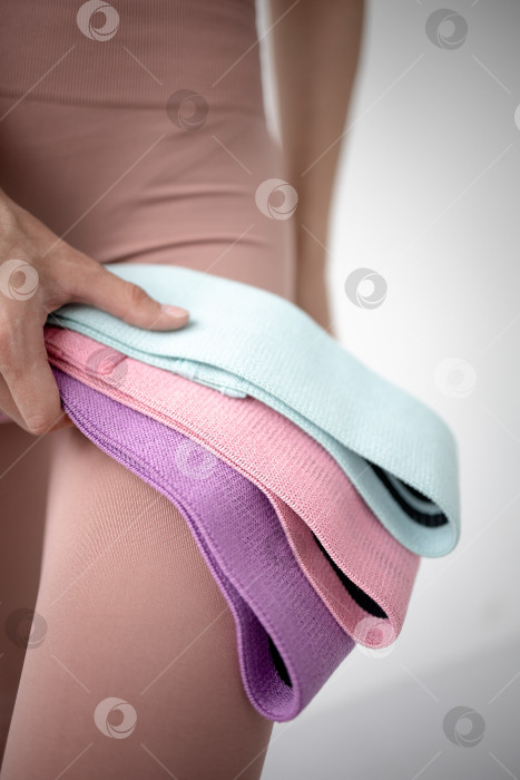 Скачать Фитнес-резинки для занятий спортом в руках девушки. На снимке крупным планом женские руки натягивают синюю спортивную резинку для тренировки мышц тела в тренажерном зале фотосток Ozero