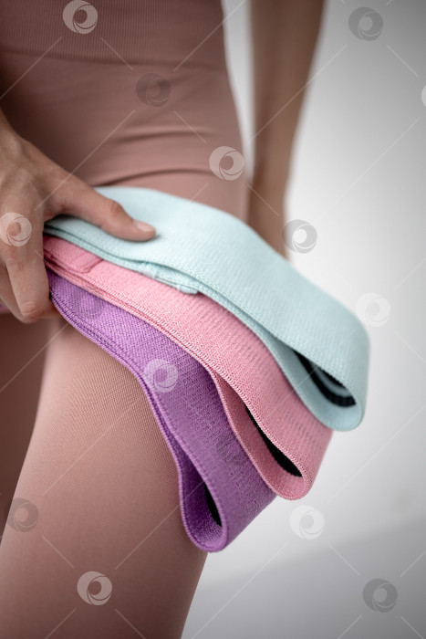 Скачать Фитнес-резинки для занятий спортом в руках девушки. На снимке крупным планом женские руки натягивают синюю спортивную резинку для тренировки мышц тела в тренажерном зале фотосток Ozero