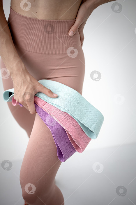 Скачать Фитнес-резинки для занятий спортом в руках девушки. На снимке крупным планом женские руки натягивают синюю спортивную резинку для тренировки мышц тела в тренажерном зале фотосток Ozero