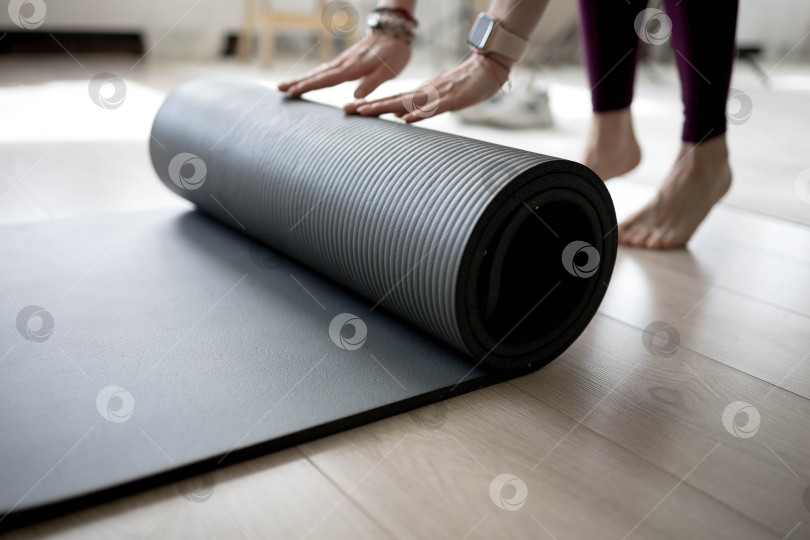Скачать девушка сворачивает коврик для фитнеса. девушка раскладывает коврик для упражнений в фитнес-студии. Он занимается медитацией и йогой, растягивая свое тело для поддержания здоровья фотосток Ozero