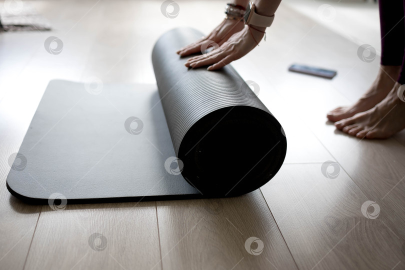 Скачать девушка сворачивает коврик для фитнеса. девушка раскладывает коврик для упражнений в фитнес-студии. Он занимается медитацией и йогой, растягивая свое тело для поддержания здоровья фотосток Ozero