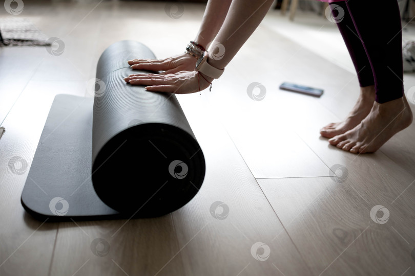 Скачать девушка сворачивает коврик для фитнеса. девушка раскладывает коврик для упражнений в фитнес-студии. Он занимается медитацией и йогой, растягивая свое тело для поддержания здоровья фотосток Ozero