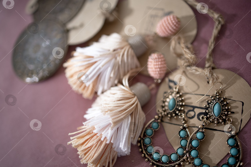 Скачать Набор ручной работы из зеленой, золотистой, бронзовой, слоновой кости и бордовой бижутерии с драгоценными камнями, кисточками, кристаллами и перьями на фоне дерева, фотосток Ozero