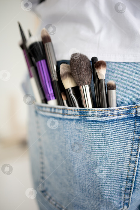 Скачать кисточки для макияжа, торчащие из кармана синих джинсов на ярком белом фоне. профессиональный визажист. нанесение макияжа. косметические процедуры фотосток Ozero
