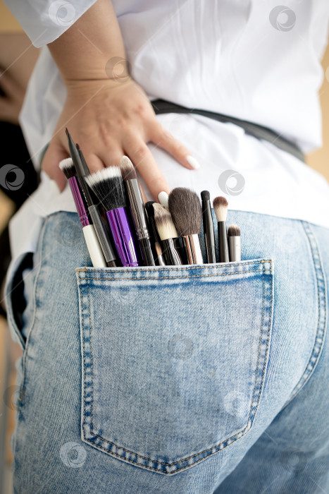 Скачать кисточки для макияжа, торчащие из кармана синих джинсов на ярком белом фоне. профессиональный визажист. нанесение макияжа. косметические процедуры фотосток Ozero
