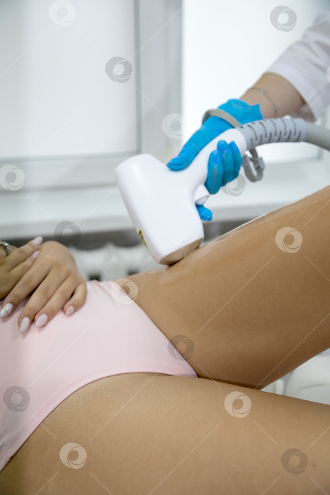 Скачать Процедура удаления волос. На кадре молодая подтянутая клиентка, проходящая процедуру лазерной эпиляции тела в клинике красоты. Концепция женской красоты и косметологии фотосток Ozero