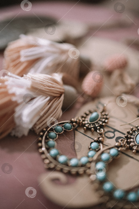 Скачать Набор ручной работы из зеленой, золотистой, бронзовой, слоновой кости и бордовой бижутерии с драгоценными камнями, кисточками, кристаллами и перьями на фоне дерева, фотосток Ozero