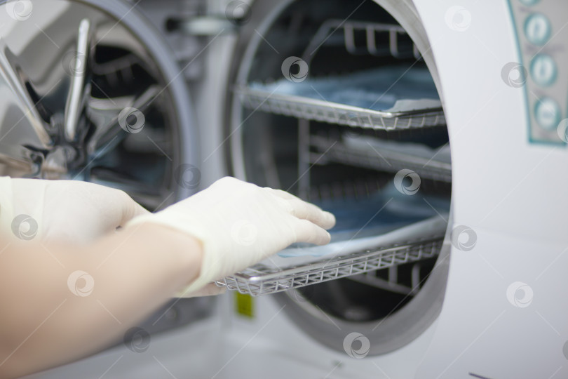 Скачать Автоклавное устройство для стерилизации медицинских изделий, с помощью которого используются инструменты. Рука рабочего вводит инструменты внутрь. фотосток Ozero