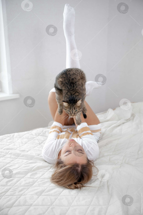Скачать Женщина и кошка лежат на кровати на белом покрывале фотосток Ozero